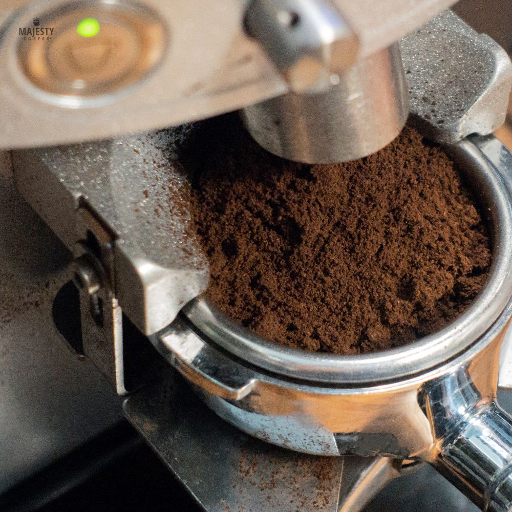Portafilter filled with fresh espresso grounds under a grinder